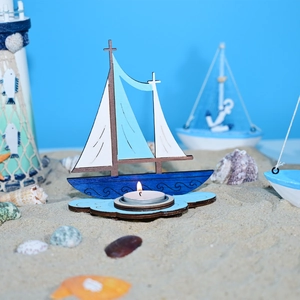 Détail d'un bougeoir voilier en bois sur du sable avec des coquillages et étoiles de mer