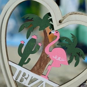 Macro detail of wooden heart pendant with pink flamingo and palm tree tropical motifs