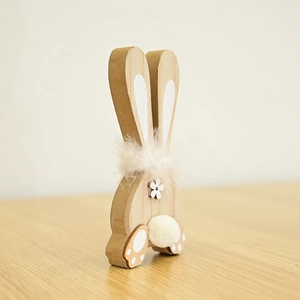 Close-up of wooden bunny decor with white flower, feather neckband and fluffy pom pom tail