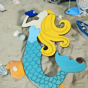 Detail of wooden mermaid wall decor with blue tail on beach sand and seashells