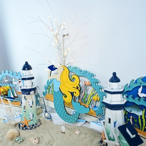 Detail of wooden mermaid and lighthouse decor pieces on a miniature sand beach setup