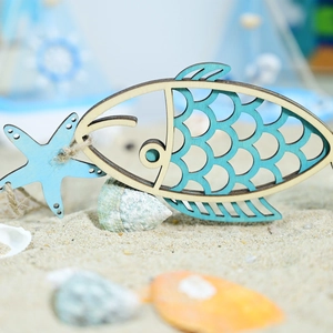 Detail of wooden fish and starfish decor with blue paint on a sandy beach background