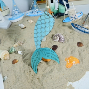Detail of wooden mermaid tail pendant with blue scale texture in beach sand setting