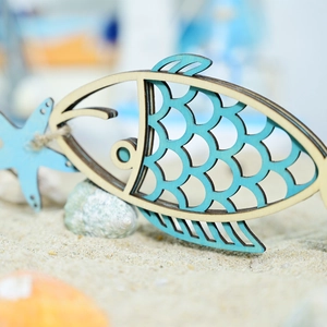 Detail of wooden fish ornament with blue scale pattern on white sand with seashells