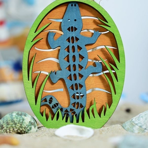 Detail of laser-cut multi-layer wooden lizard decor on sand with natural seashells