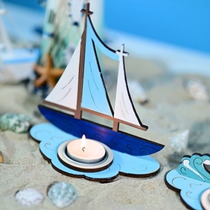 Détail du bougeoir voilier nautique bleu et blanc posé sur un décor de sable et coquillages