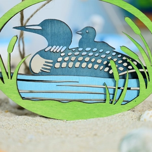 Macro detail of laser-cut layered wood loon hanging decor with blue water and reed accents
