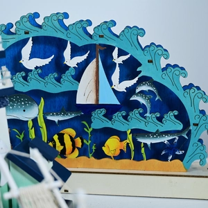 Dettaglio lampada LED in legno a tema marino con barca a vela e balena stile mediterraneo