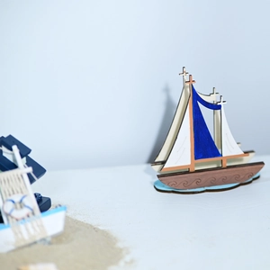 Detail of wooden sailboat model with blue and white sails on a wave-shaped base
