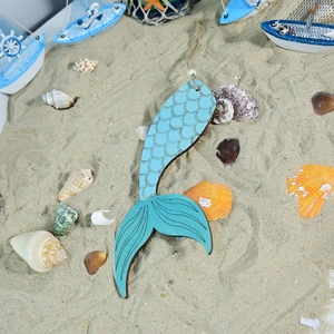 Detail of wooden mermaid tail pendant with blue scales and rustic hemp rope on sand