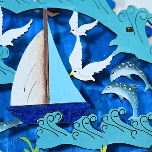 Dettaglio decorazione marina in legno a strati con barca a vela blu e gabbiani a LED
