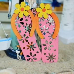 Detail of flip-flop wooden hanging sign with hollow flower patterns on sandy beach