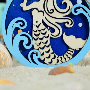 Detail of multi-layered wooden mermaid plaque on beach sand with sea shells decor