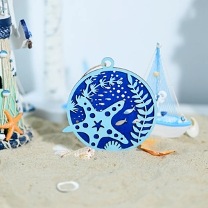 Detail of round laser-cut wooden nautical decor with starfish and fish on a sand background