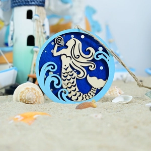 Detail of laser-cut wooden mermaid wall hanging with natural jute rope on a beach setting