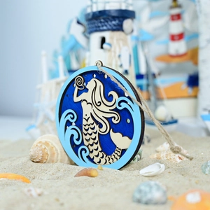 Close-up of wooden mermaid wall hanging on beach sand with natural seashells
