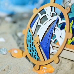 Detail of wooden ship wheel anchor ornament with sailboat and seagull on beach sand