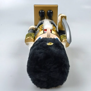 Top down view of a black and gold nutcracker soldier with a fuzzy hat and golden base