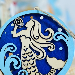 Macro detail of laser-cut wooden mermaid wall decor showing layered blue sea waves