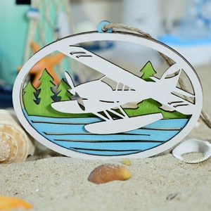 Detail eines ovalen Holzschilds mit Wasserflugzeug und Kieferndesign auf Sandstrand
