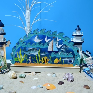 Dettaglio della lampada oceanica in legno 3D con balena e barca a vela sulla spiaggia