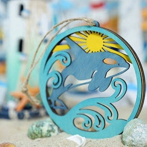 Detail of wooden round ornament featuring an ocean orca and sun carving with hanging rope