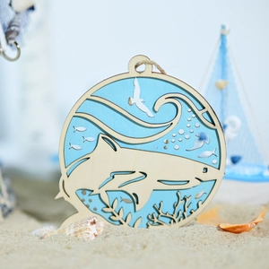 Close-up of laser-cut wooden ocean ornament featuring a shark and coral on a sandy beach