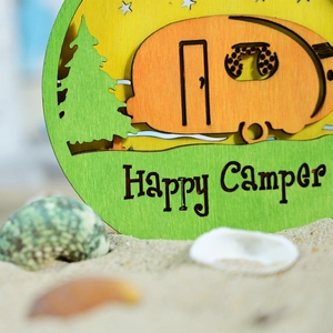 Macro detail of wooden Happy Camper sign featuring a vintage camper and pine tree design