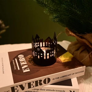 Detail of black metal house silhouette candle holder on books with warm candlelight