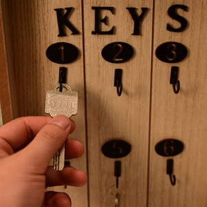 Close-up of hand placing a key on vintage wooden organizer rack with numbered hooks