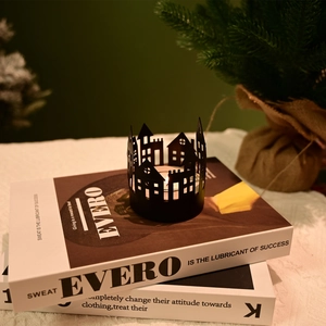 Detail of a black hollow architectural candle holder with a burning tea light on books