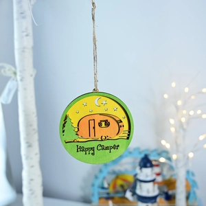 Detail of Happy Camper round wooden wall hanging with pine trees and caravan scene