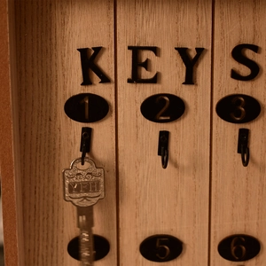 Detail of wooden key organizer with black 'KEYS' text and numbered metal hooks on wall