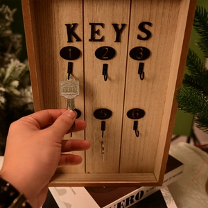 Close-up of hand hanging keys on a wooden wall organizer with six numbered metal hooks