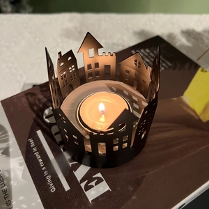 Close-up of black metal candle holder with house silhouette and warm tea light candle