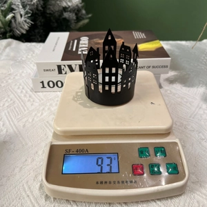 Detail shot of a black metal cutout house candle holder weighing 93g on a scale