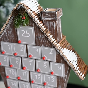 Close-up of a rustic wooden house advent calendar with 25 gray numbered drawers