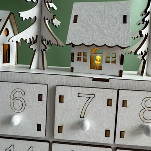 Detail of white wooden advent calendar with LED lighted cabin and numbered drawers