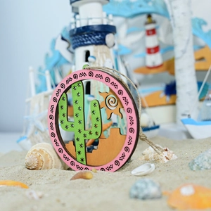 Macro detail of round wooden desert plaque with cactus and sun on a beach sand background