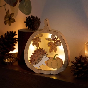 Détail d'une lampe citrouille en bois avec LED et gravures de feuilles et d'un hérisson