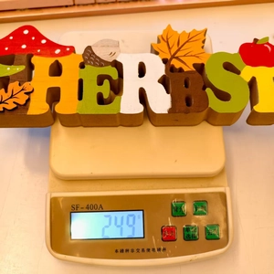 Detail shot of the autumn themed wooden Herbst sign weighing 249g on a digital scale