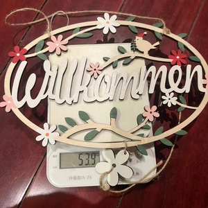 Close-up of wooden Willkommen sign with flowers and bird on a digital scale weighing 53.9g