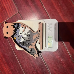 Close-up of a laser-cut wooden owl ornament showing detailed Halloween ghost scenes
