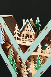 Detailed side view showing 3D laser-cut layers of wooden Christmas forest and cabin