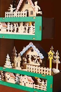 Detailed laser-cut wooden Christmas scene with layered snowy cottages and pine trees