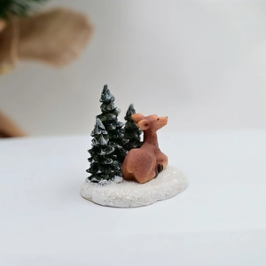 Détail d'un cerf en résine brune sur base enneigée avec pins miniatures effet givré