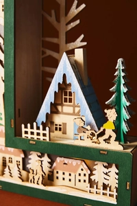 Detailed close-up of a multilayered laser-cut wooden Christmas scene with snowy cabins