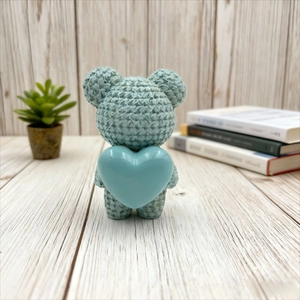 Cute light blue resin bear figurine with knitted texture holding a smooth heart ornament