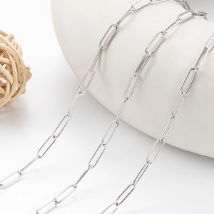 Collier chaîne trombone en acier poli drapé sur un vase décoratif en céramique blanche