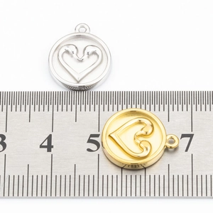 Dettaglio macro di ciondoli a cuore da 1,5 cm in acciaio inox oro e argento con righello